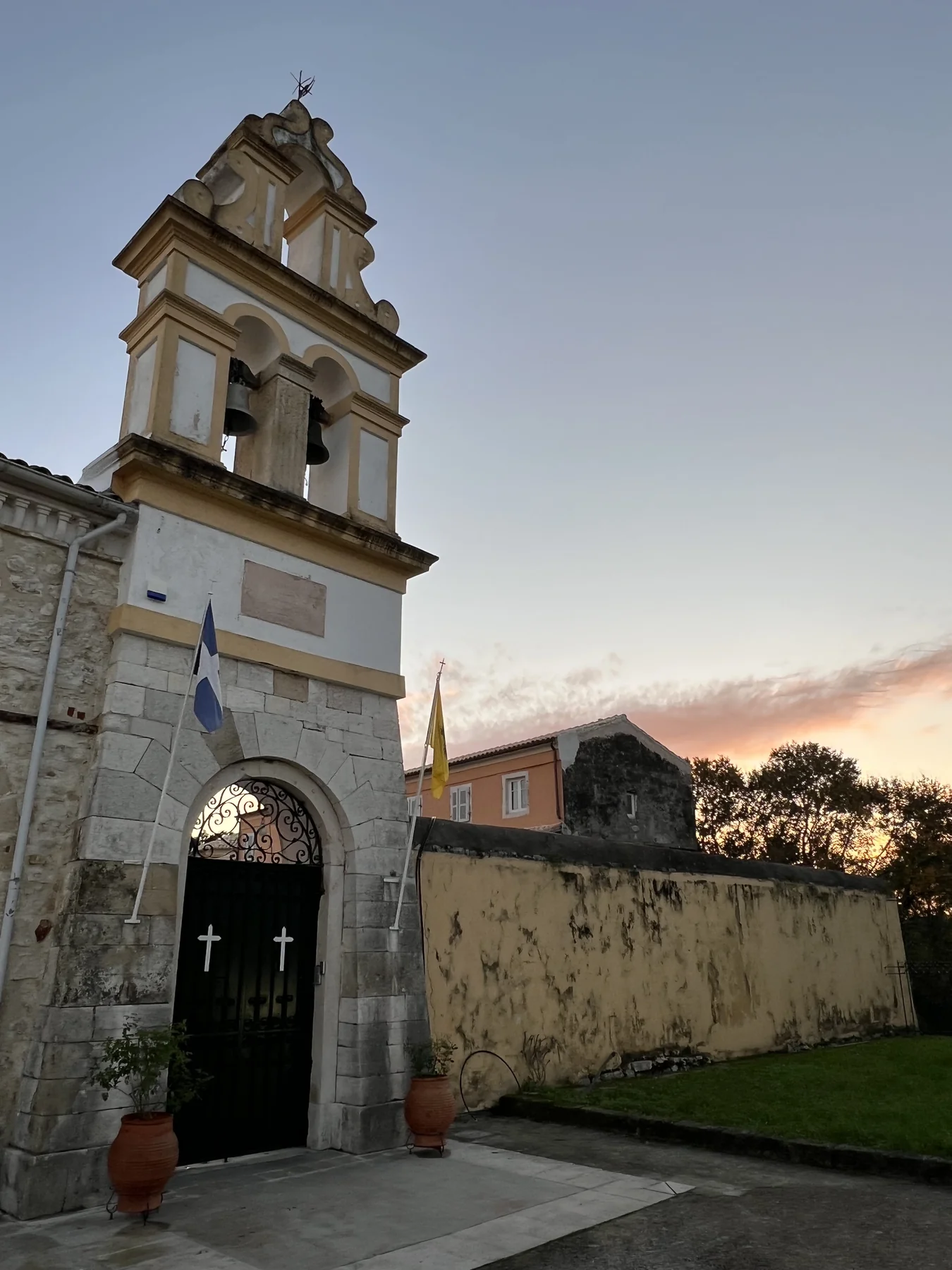 Church belfry at dusk, Greek and papal flags, pink sky
