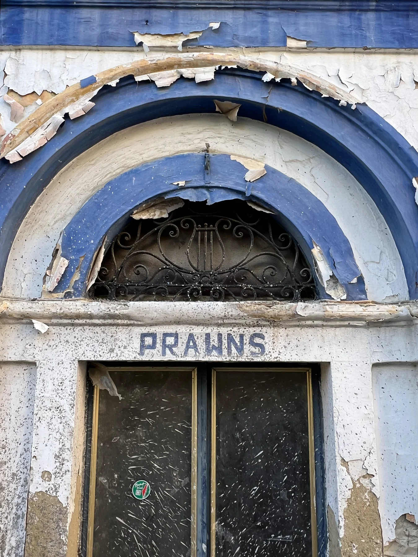 Peeling paint on arched doorway — the word PRAWNS in faded blue letters
