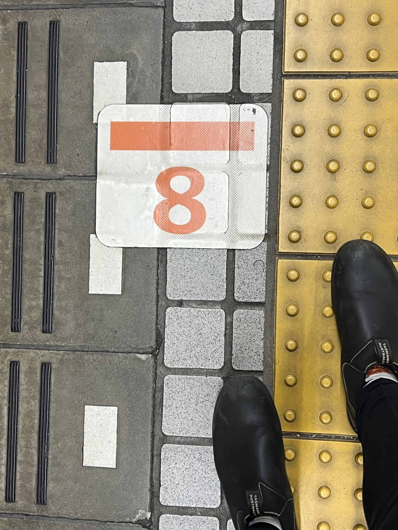 Found 8 — orange numeral on station platform, tactile paving, boots